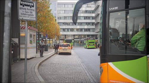 Ein Bus fährt in den zentralen Omnibusbahnhof (ZOB) ein. Im Hintergrund steht Herr Werdermann mit einem Zettel in der Hand, bereit, die Einfahrtsgebühr zu kassieren.